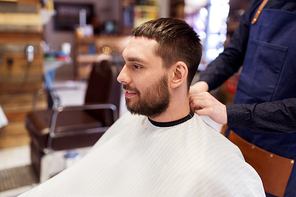 grooming, hairdressing and people concept - hairdresser or barber and man in cape with beard at barbershop