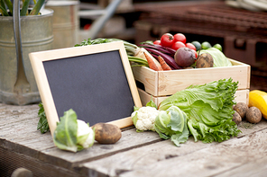 harvest, food and agriculture concept - close up of vegetables with chalkboard on farm