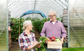 farming, gardening, agriculture, harvesting and people concept - senior couple with box of vegetables and clipboard at farm greenhouse