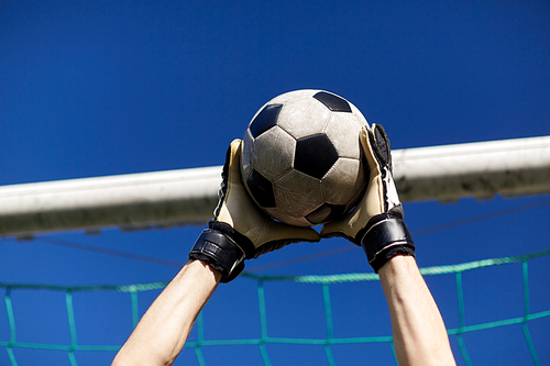 sport and people - soccer player or goalkeeper hands catching ball at football goal over blue sky