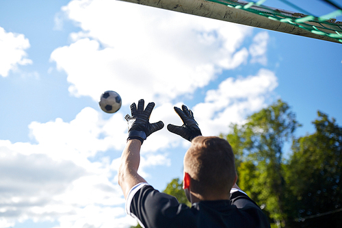 sport and people - soccer player or goalkeeper catching ball at football goal on field