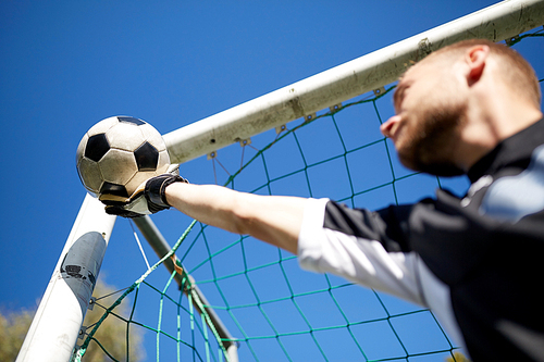 sport and people - soccer player or goalkeeper catching ball at football goal on field