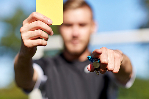 sport, caution, game and people - referee with whistle showing yellow card on football field