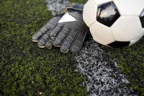 sport, soccer and game - ball and goalkeeper gloves on football field