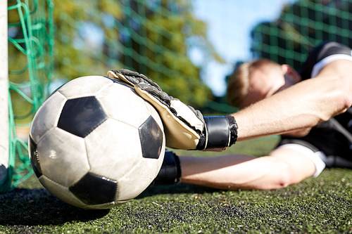 sport and people - soccer player or goalkeeper lying with ball at football goal on field