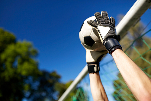 sport and people - soccer player or goalkeeper hands catching ball at football goal on field