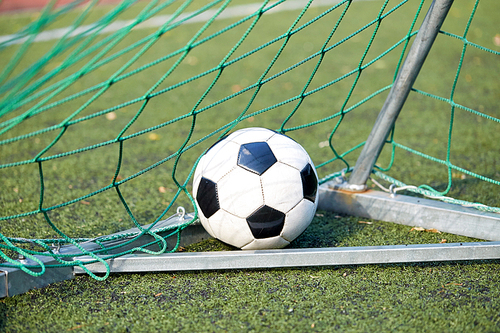 sport, soccer and game - ball at goal net on football field