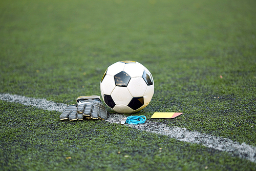 sport, soccer and game - ball, goalkeeper gloves, referee whistle and caution card on football field