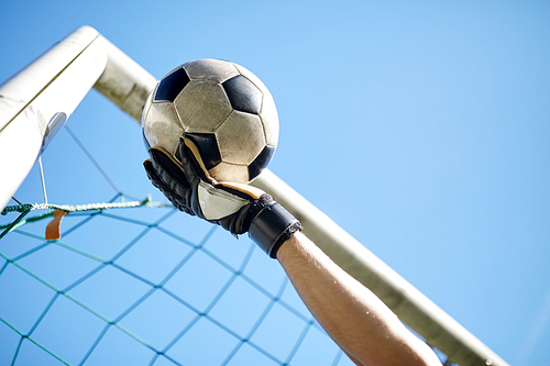 sport and people - soccer player or goalkeeper hand catching ball at football goal over blue sky