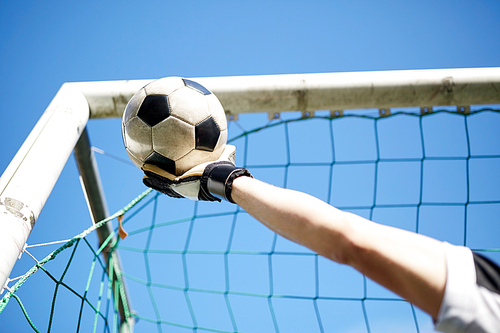 sport and people - soccer player or goalkeeper hand catching ball at football goal over blue sky