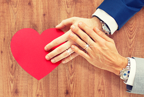 people, homosexuality, same-sex marriage, valentines day and love concept - close up of happy married male gay couple hands with red paper heart shape over wooden background