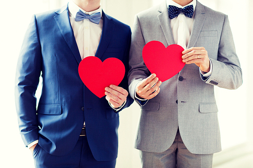 people, homosexuality, same-sex marriage, valentines day and love concept - close up of happy married male gay couple holding red paper heart shapes on wedding