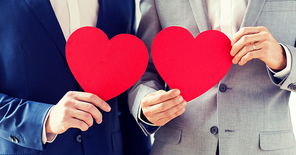 people, homosexuality, same-sex marriage, valentines day and love concept - close up of happy married male gay couple holding red paper heart shapes on wedding