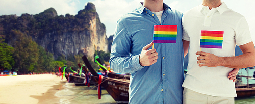 people, homosexuality, same-sex marriage, travel and love concept - close up of happy male gay couple holding  flags and hugging over thailand beach background