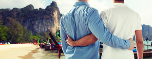 people, homosexuality, travel and love concept - close up of happy male gay couple hugging from back over thailand beach background