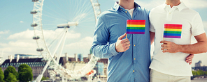 people, homosexuality, same-sex marriage, travel and love concept - close up of happy male gay couple holding rainbow flags and hugging from back over london ferry wheel background