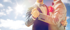 people, homosexuality, same-sex marriage and love concept - close up of happy male gay couple holding hands and dancing on wedding over sky and sun background