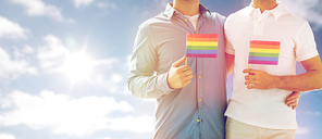 people, homosexuality, same-sex marriage and love concept - close up of happy male gay couple hugging and holding rainbow flags over sky and sun background