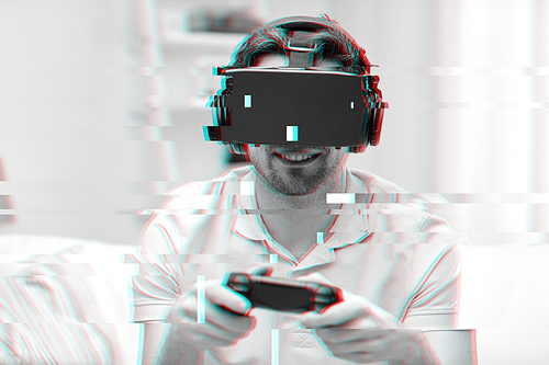 technology, gaming, entertainment and people concept - happy young man with virtual reality headset or 3d glasses and gamepad controller playing video game  at home over glitch effect