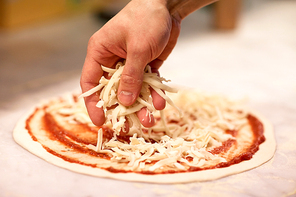 food, culinary, italian cuisine, people and cooking concept - cook hand adding grated cheese to pizza at pizzeria
