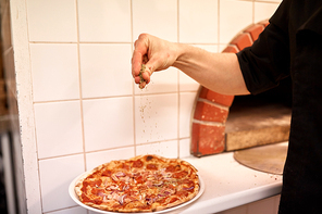 food, culinary, italian cuisine, people and cooking concept - cook hand adding pepper to salami pizza at pizzeria