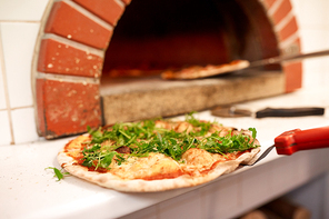 food, italian kitchen, culinary and cooking concept - baked pizza with arugula on peel at pizzeria oven