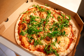 fast food, italian cuisine, takeaway and eating concept - close up of pizza with arugula in paper box on table at pizzeria