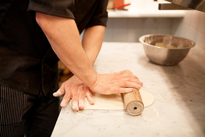 cooking, baking and people concept - close up of male chef with rolling-pin rolling dough at restaurant or bakery kitchen