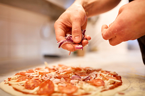 food, culinary, italian cuisine, people and cooking concept - cook hands adding red onion to salami pizza at pizzeria