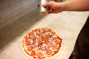 food, culinary, italian cuisine, people and cooking concept - cook hand adding pepper to salami pizza at pizzeria