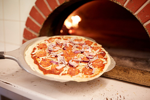 food, italian kitchen, culinary, baking and cooking concept - peel placing pizza into oven at pizzeria