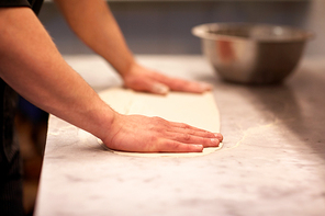 cooking, baking and people concept - chef hands preparing dough on table at kitchen
