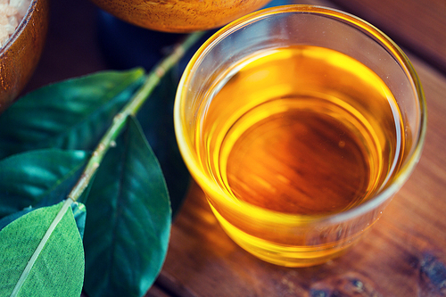 beauty, spa, body care, natural cosmetics and wellness concept - close up of honey in glass cup with leaves on wooden table
