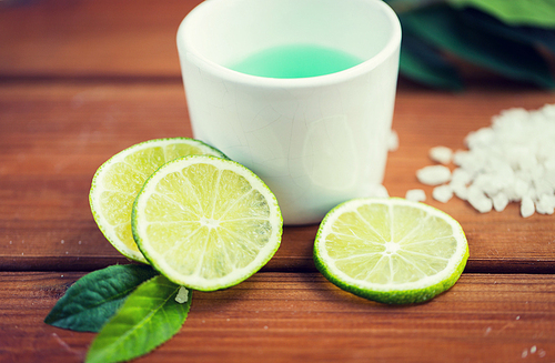 beauty, spa, body care, natural cosmetics and wellness concept - close up of citrus body lotion in cup and 씨솔트 with limes on wooden table