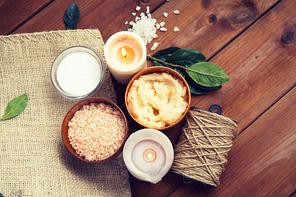 beauty, spa, therapy, natural cosmetics and wellness concept - close up of body scrub with  himalayan pink salt and candles on wood