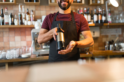 small business, alcohol, people and service concept - happy man or bartender with bottle of wine at restaurant bar