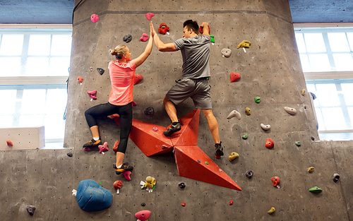 fitness, extreme sport, bouldering, people and healthy lifestyle concept - man and woman exercising at indoor climbing gym and making high five gesture