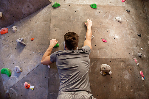 fitness, extreme sport, bouldering, people and healthy lifestyle concept - young man exercising at indoor climbing gym wall