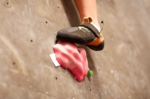 fitness, extreme sport, bouldering, people and equipment concept - foot of young woman in rock shoe on indoor climbing gym wall holds
