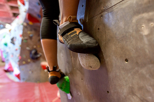 fitness, extreme sport, bouldering, people and healthy lifestyle concept - feet of young woman exercising at indoor climbing gym