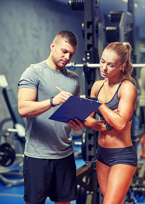fitness, sport, exercising and diet concept - young woman and personal trainer with clipboard writing exercise plan in gym