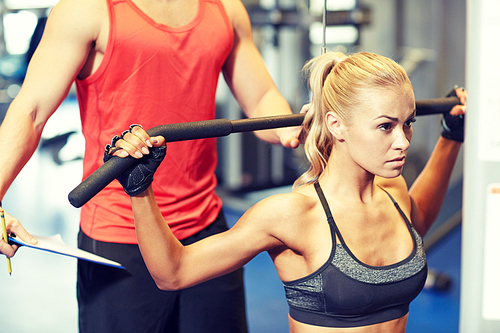 sport, fitness, teamwork and people concept - young woman and personal trainer flexing muscles on gym machine