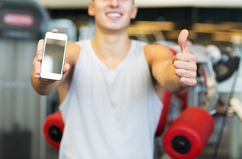 sport, bodybuilding, lifestyle, technology and people concept - close up of happy young man showing thumbs up and smartphone blank screen in gym