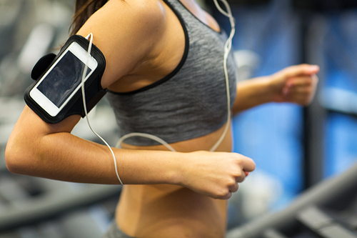 sport, fitness, technology and lifestyle concept - close up of woman with smartphone or player and earphones exercising on treadmill in gym, motion blurred, out of focus image
