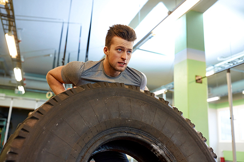 strongman, bodybuilding, sport, fitness and people concept - young man doing tire flip at training in gym