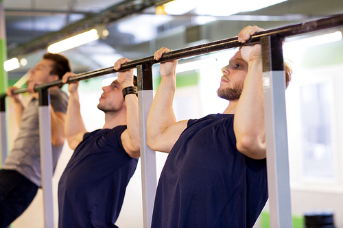 sport, fitness, exercising and people concept - group of young men doing pull-ups on horizontal bar in gym