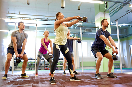 sport, fitness, weightlifting and training concept - group of people with kettlebells exercising in gym