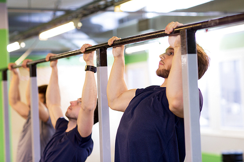 sport, fitness, exercising and people concept - group of young men doing pull-ups on horizontal bar in gym