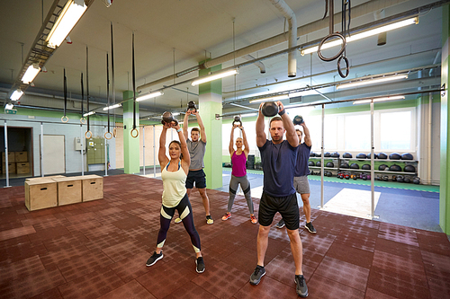 sport, fitness, weightlifting and training concept - group of people with kettlebells and heart-rate trackers exercising in gym