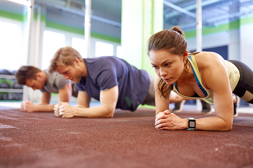 fitness, sport, exercising and people concept - woman with heart-rate tracker at group training doing plank exercise in gym